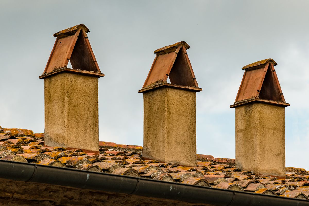 Three chimneys fitted with protective caps on a tiled roof