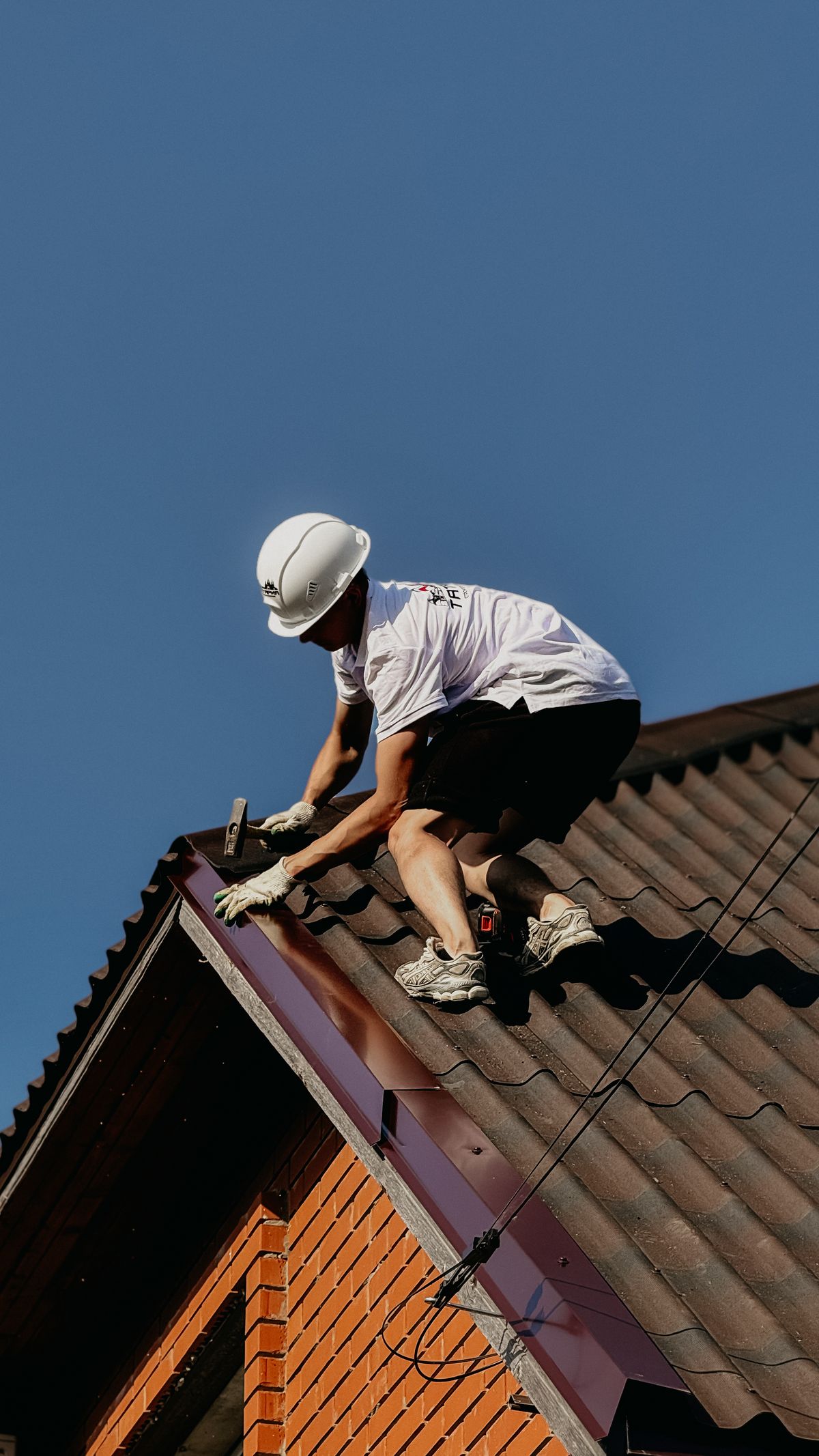 Roofer in a safety helmet working on a brick house roof