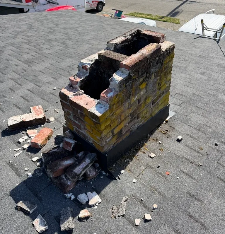 A crumbling brick chimney before rebuild, with loose bricks removed and stacked on the roof