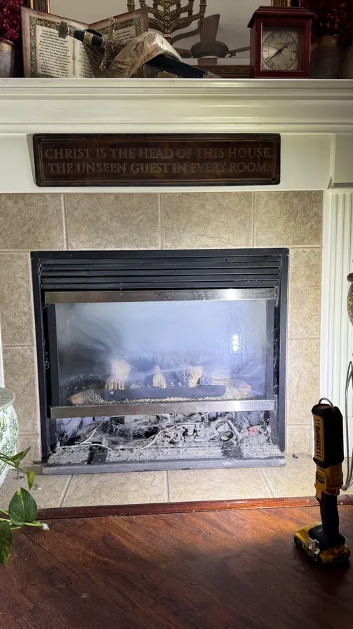 A gas fireplace with sooty glass and a dirty firebox before cleaning